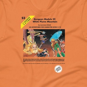 May include: Orange t-shirt with a Dungeons & Dragons module cover printed on the front. The cover features a fantasy illustration of a group of adventurers fighting a monstrous creature. The text on the cover reads "Dungeon Module 52 White Plume Mountain by Lawrence Schick An Adventure for Character Levels 3-10".