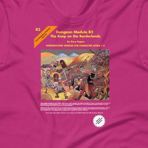 May include: A magenta t-shirt featuring the text "Dungeon Module B2 The Keep on the Borderlands" with an illustration of a fantasy battle scene. The shirt is a short-sleeved crew neck.