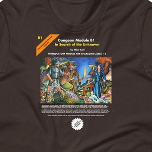 以下が含まれることがあります： ダンジョンズ＆ドラゴンズ モジュールカバーのグラフィックがプリントされた茶色のTシャツ。カバーには、ファンタジーの世界にいる冒険者たちのグループが描かれている。カバーのテキストには、「Dungeon Module 81 In Search of the Unknown by Mike Carr INTRODUCTORY MODULE FOR CHARACTER LEVELS 1-3」と記載されている。