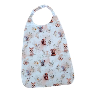 Puede incluir: Un babero para bebé con fondo blanco, con un estampado de animales de dibujos animados y elementos florales en colores suaves. El babero tiene una base redondeada y una banda para el cuello fruncida.