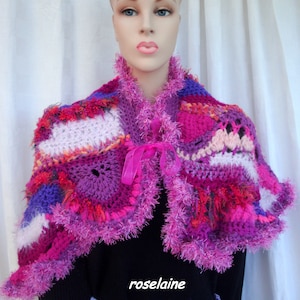 Peut inclure: Un châle crocheté rose, violet et blanc avec une bordure rose moelleuse. Le châle est porté par un mannequin avec un chemisier noir et une jupe violette clair.