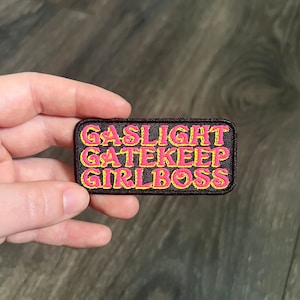 May include: A black embroidered patch with the words "Gaslight Gatekeep Girlboss" in pink lettering with yellow outlines.