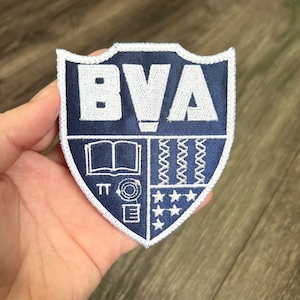 May include: A blue and white embroidered patch with the letters "BVA" in white. The patch features a book, a compass, stars, and a pattern of wavy lines.