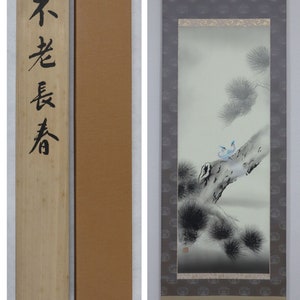 以下が含まれることがあります： 木箱と茶色の紙箱が付属した、鳥が木の枝に止まっている様子を描いた日本の巻物絵。巻物の配色は、黒、グレー、白を基調としたニュートラルカラー。木箱には黒い日本語の文字が書かれています。