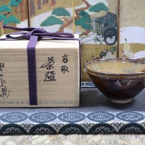 May include: A white ceramic mug with a black handle and the text "But First, Coffee" in a bold, black font. The mug is set against a blurred background, suggesting a cosy setting.