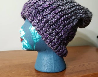 May include: Purple and gray knitted beanie hat on a blue mannequin head. The hat is slouchy and has a textured knit.