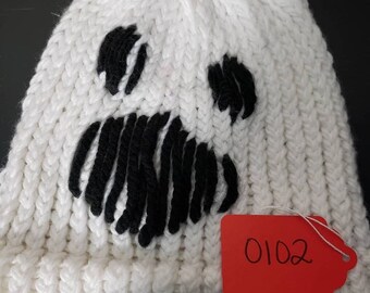 Op de afbeelding: Witte gebreide beanie met een zwart spookgezicht. De beanie heeft een label met het nummer 0102.
