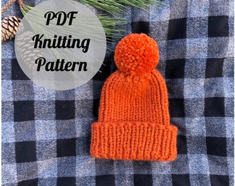 May include: An orange knitted beanie with a large pom-pom on top. The hat is made of thick yarn and has a folded brim. The text "PDF Knitting Pattern" is overlaid on the image.