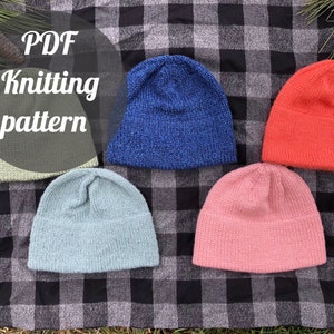 Op de afbeelding: Vijf gebreide mutsen in verschillende kleuren: lichtgroen, blauw, koraal, lichtblauw en roze. De mutsen worden getoond op een zwart-wit geruit oppervlak. De tekst in de afbeelding luidt "PDF Knitting pattern".