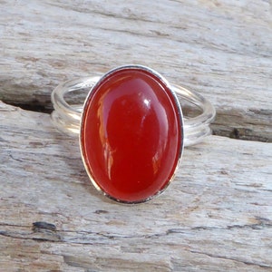 Puede incluir: Un anillo de plata con una piedra ovalada roja engastada en un engaste de bisel.