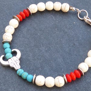 Può includere: Un braccialetto con perline bianche, rosse e turchesi con un ciondolo a forma di teschio d'argento. Il braccialetto ha una chiusura a moschettone.