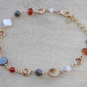 May include: A gold chain bracelet with a variety of colorful beads, including white, orange, brown, and black. The bracelet has a clasp closure.