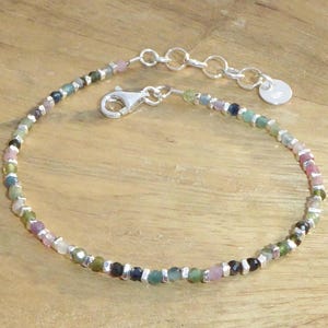 Può includere: Un braccialetto d'argento con una catena e una chiusura. Il braccialetto è decorato con piccole pietre preziose colorate in tonalità di rosa, verde e blu.