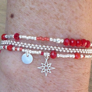 May include: A layered bracelet with silver beads and red glass beads. The bracelet has a silver charm in the shape of a star and a silver disc charm.