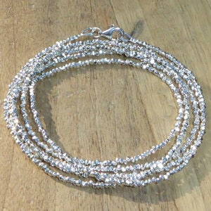 Könnte beinhalten: Eine silberne Kettenkette aus kleinen, facettierten Perlen. Die Kette ist geschichtet und hat einen Karabinerverschluss.