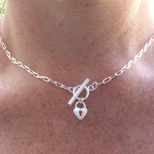 Peut inclure: Un collier en chaîne argent avec un pendentif en forme de cadenas en forme de cœur et un fermoir à glissière.