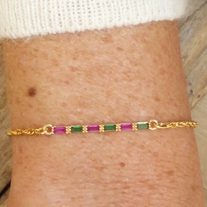 May include: A gold chain bracelet with alternating pink and green square-shaped gemstones.