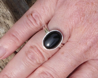 Op de afbeelding: Een zilveren ring met een zwarte ovale edelsteen. De ring zit aan een vinger.