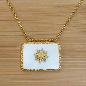 Può includere: Una collana con catena dorata con un ciondolo quadrato bianco con un design a forma di sole dorato.