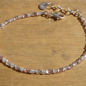 May include: A delicate silver bracelet with a clasp closure. The bracelet is made with small, faceted, clear and pink beads.