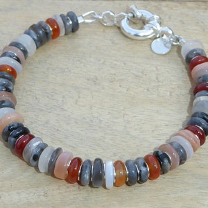 May include: A silver bracelet with a clasp and a variety of gemstone beads in shades of gray, white, orange, and red.