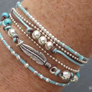 Peut inclure: Un ensemble de bracelets avec des perles turquoise et argent, un pendentif en forme de plume argentée et un cordon marron.