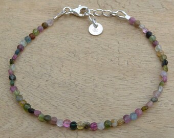 May include: A delicate bracelet made with small, colorful gemstone beads. The beads are a mix of pink, green, blue, and brown. The bracelet is secured with a silver clasp.