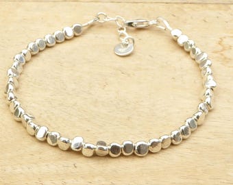 May include: A silver bracelet featuring a series of small, irregular, rounded beads strung together. The bracelet has a delicate chain and clasp closure, with a small, round charm near the clasp. The beads are approximately 0.25 inches in diameter.
