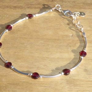 Puede incluir: Una pulsera de plata con una cadena delicada y detalles de piedras preciosas rojas.