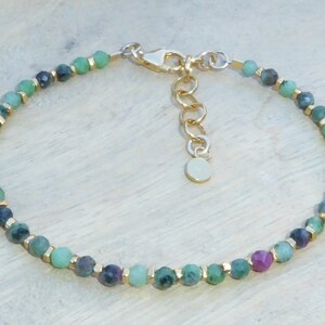 May include: A gold chain bracelet with green and pink gemstone beads. The bracelet has a lobster clasp closure.