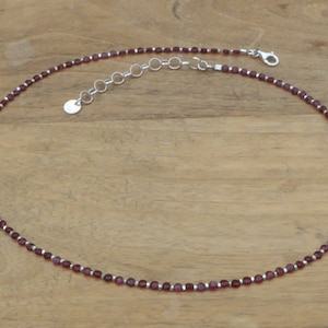 Può includere: Una delicata collana a catena d'argento con piccole perline viola scuro. La collana ha una chiusura a moschettone e un piccolo ciondolo rotondo in argento.