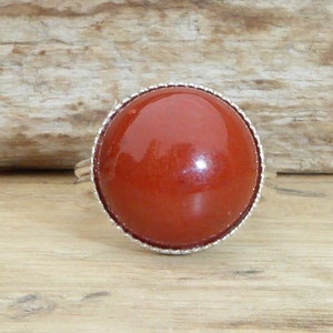 Op de afbeelding: Een zilveren ring met een grote, ronde, rode edelsteen in een bezel-setting.