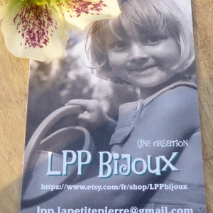 K&ouml;nnte beinhalten: Eine Visitenkarte mit einem Schwarz-Wei&szlig;-Foto eines Kindes, dem Text "LPP Bijoux" und einer Website-Adresse. Eine wei&szlig;-gr&uuml;ne Blume mit kastanienbraunen Flecken befindet sich in der oberen linken Ecke.