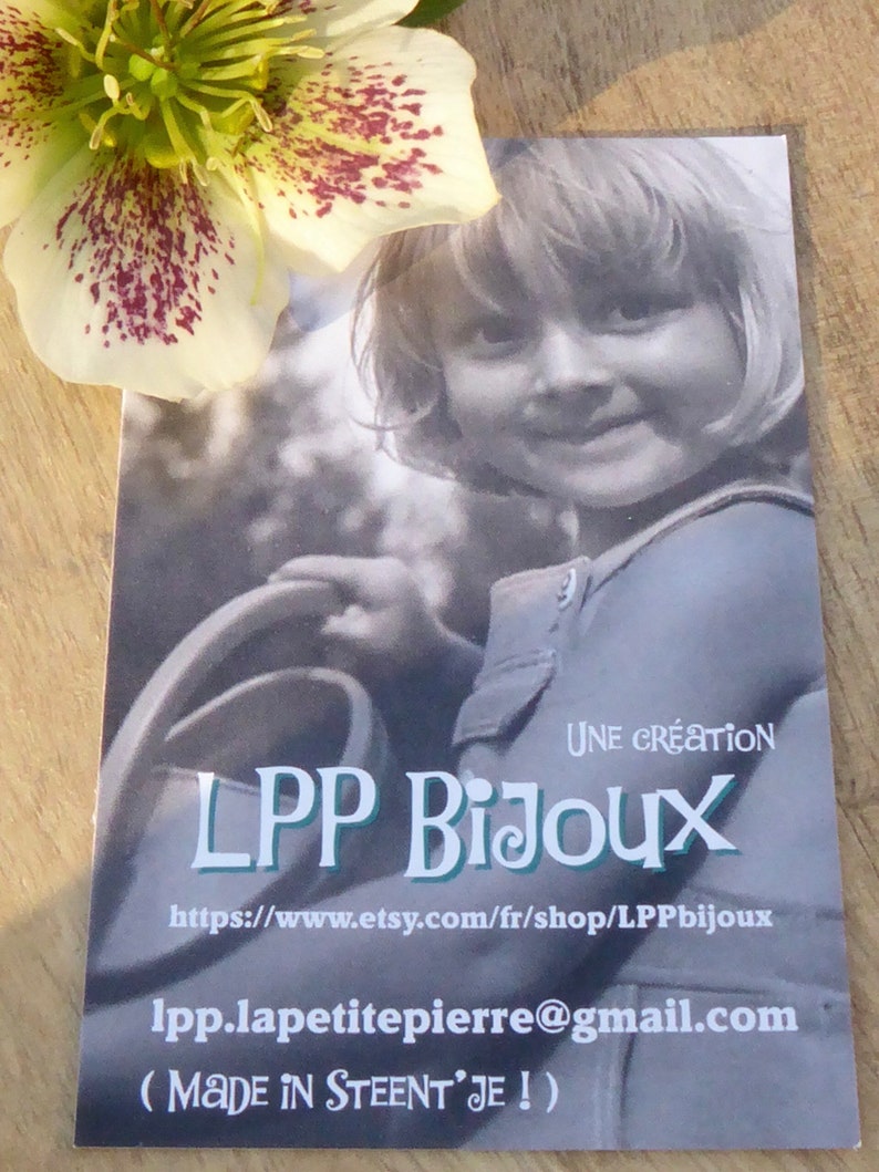 K&ouml;nnte beinhalten: Eine Visitenkarte mit einem Schwarz-Wei&szlig;-Foto eines Kindes, dem Text "LPP Bijoux" und einer Website-Adresse. Eine wei&szlig;-gr&uuml;ne Blume mit kastanienbraunen Flecken befindet sich in der oberen linken Ecke.