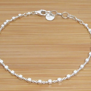 Peut inclure: Un bracelet en argent avec une chaîne composée de petits maillons carrés.