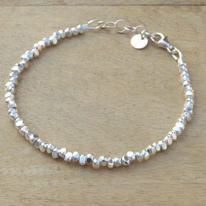 Op de afbeelding: Een zilveren armband met een delicate ketting en kleine, getextureerde kralen.