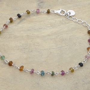 May include: A delicate bracelet with a silver chain and small, colourful gemstones. The gemstones are in shades of pink, green, brown, and black. The bracelet has a lobster clasp and an adjustable chain.