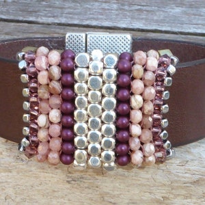 Peut inclure: Un bracelet jonc en cuir marron avec un design de perles argentées et multicolores. Les perles sont dans des tons de rose, marron et violet.