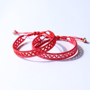 Peut inclure: Deux bracelets tressés rouges avec un motif géométrique. Les bracelets sont faits d'un cordon rouge fin et ont un design délicat et complexe.