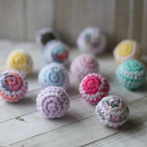 May include: A collection of colorful crocheted balls in various shades of pink, purple, blue, green, yellow, and white. The balls are made with a textured yarn and have a variety of patterns.