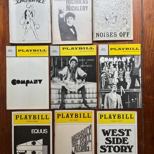May include: Nine vintage Playbill theater programs with yellow and black covers are arranged on a wooden surface. Titles include "Song & Dance", "The Life & Adventures of Nicholas Nickleby", "Noises Off", "Company", "Once Upon a Mattress", "Equus", "Merrily We Roll Along", and "West Side Story".