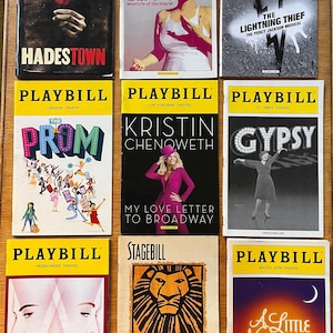 Puede incluir: Una colección de programas de mano de varios espectáculos de Broadway, incluyendo "Hadestown" y "The Lion King". Las portadas presentan ilustraciones vibrantes y títulos de espectáculos, con una pancarta amarilla en la parte superior. Incluye "War Paint" y "Gypsy".