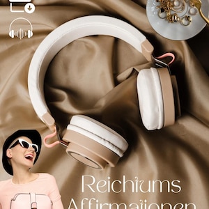 May include: White headphones with a beige headband and earcups, lying on a brown fabric surface. The text "Reichtums Affirmationen" is written in white on the fabric.  The image also includes a small plate with gold jewelry and a fork.