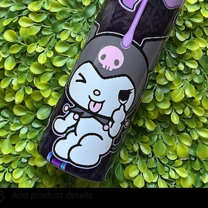 Pode incluir: Um copo preto e branco com um design de gotejamento roxo e um personagem de desenho animado com uma caveira na cabe&ccedil;a. O personagem est&aacute; piscando e mostrando a l&iacute;ngua. O copo est&aacute; em um fundo verde.