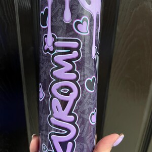 Pode incluir: Um copo de a&ccedil;o inoxid&aacute;vel roxo e preto com um design roxo que pinga e a palavra "FUROMI" em uma fonte estilizada. O copo tem um canudo e &eacute; decorado com cora&ccedil;&otilde;es e outros pequenos desenhos.