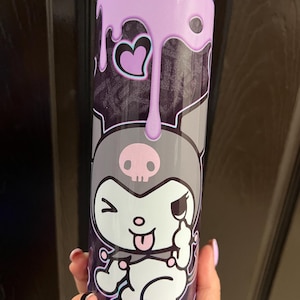 Pode incluir: Um copo de a&ccedil;o inoxid&aacute;vel com um personagem de desenho animado preto e branco com uma caveira e ossos cruzados na cabe&ccedil;a. O copo tem um design de gotejamento roxo e um cora&ccedil;&atilde;o rosa.