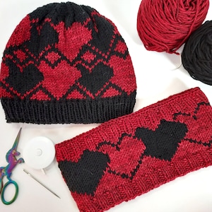May include: A black and red knit hat and headband set with a heart pattern. The hat is a beanie style and the headband is a wide band.