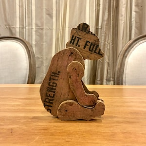 May include: A handcrafted wooden bear figurine with the words "STRENGTH" and "HT. FULL" printed on it. The bear is made from light brown wood and has a rustic, vintage appearance. It is sitting on a wooden table.