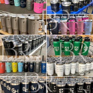 May include: A collection of various stainless steel tumblers with different designs and engravings. The tumblers are in various colours, including black, white, blue, green, pink, and grey. Some tumblers have handles, while others do not. The tumblers are arranged in rows on shelves and tables.