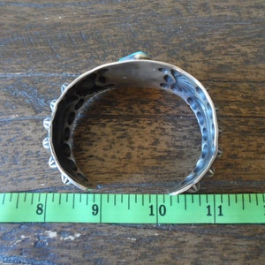 K&ouml;nnte beinhalten: Silberarmband mit T&uuml;rkis-Stein-Einlage und dekorativen Details. Das Armband hat einen Durchmesser von etwa 23 cm.